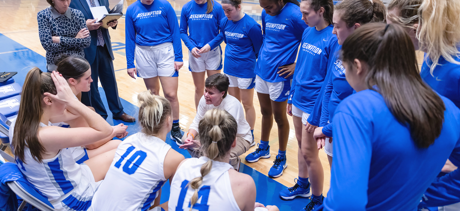Assumption University Greyhounds Women's Basketball Coach Kerry Phayre surrounded by players during a game.