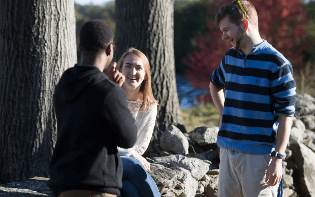 Assumption students talk near a stone wall on campus