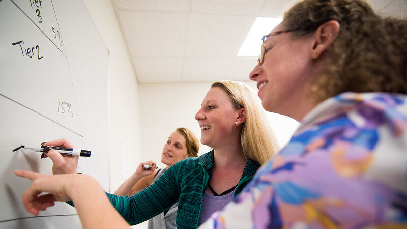 Professor and students writing on a whiteboard.