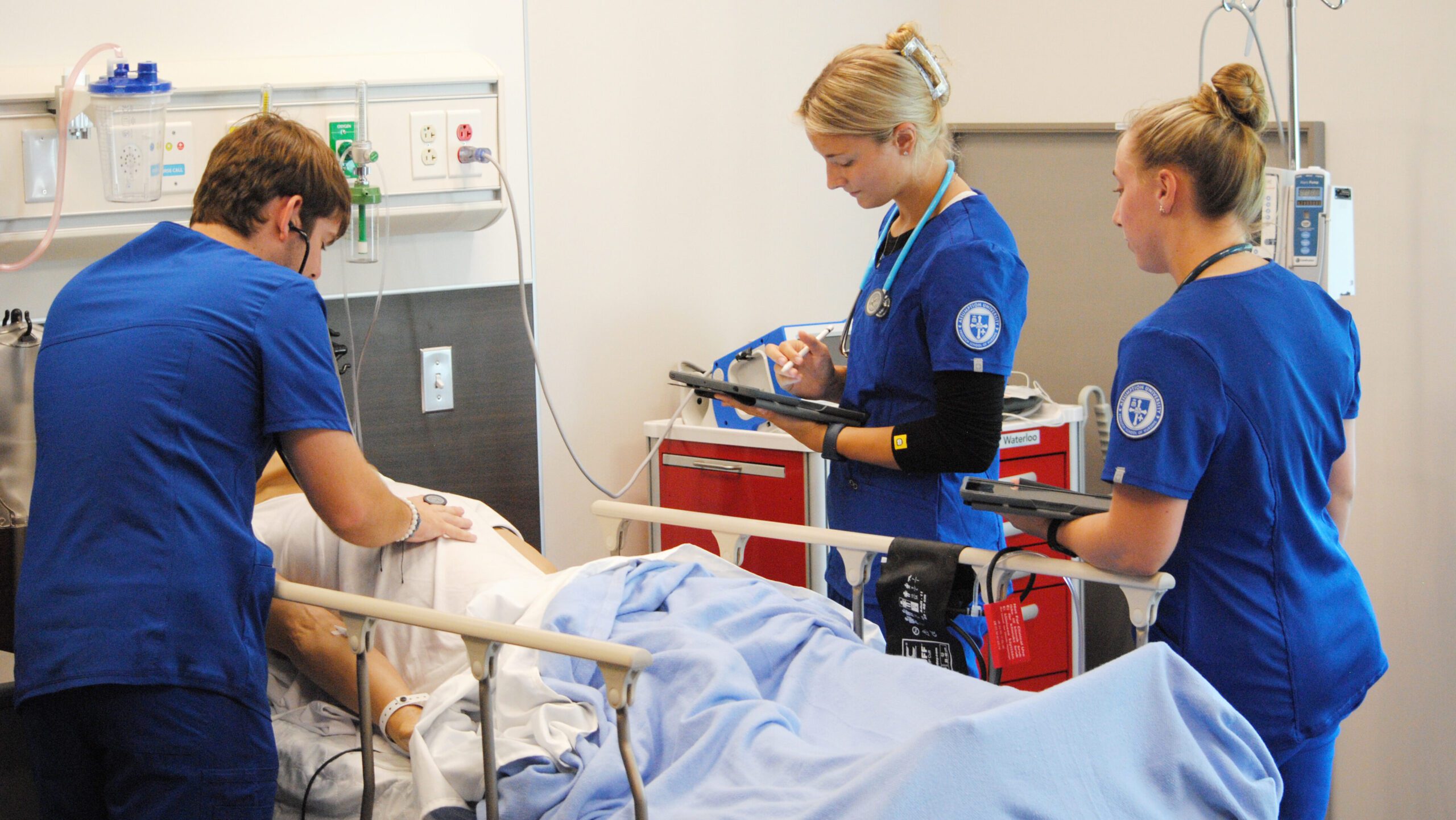 Three nursing students standing around a hospital bed