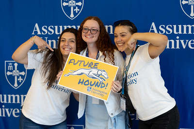 Group of three females smiling as one holds an Assumption sign.