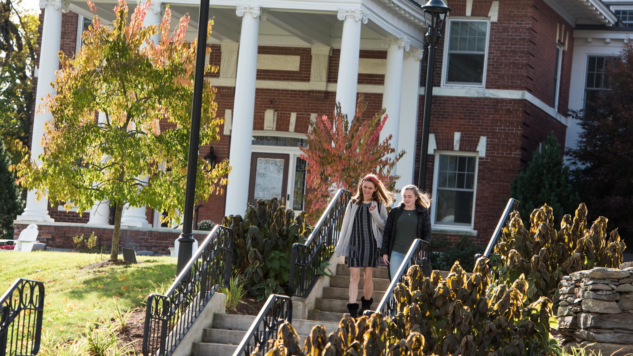 two students walking outside by the Admissions House at Assumption.