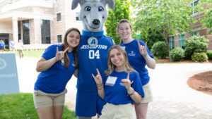Three students smiling next to the Assumption mascot Pierre