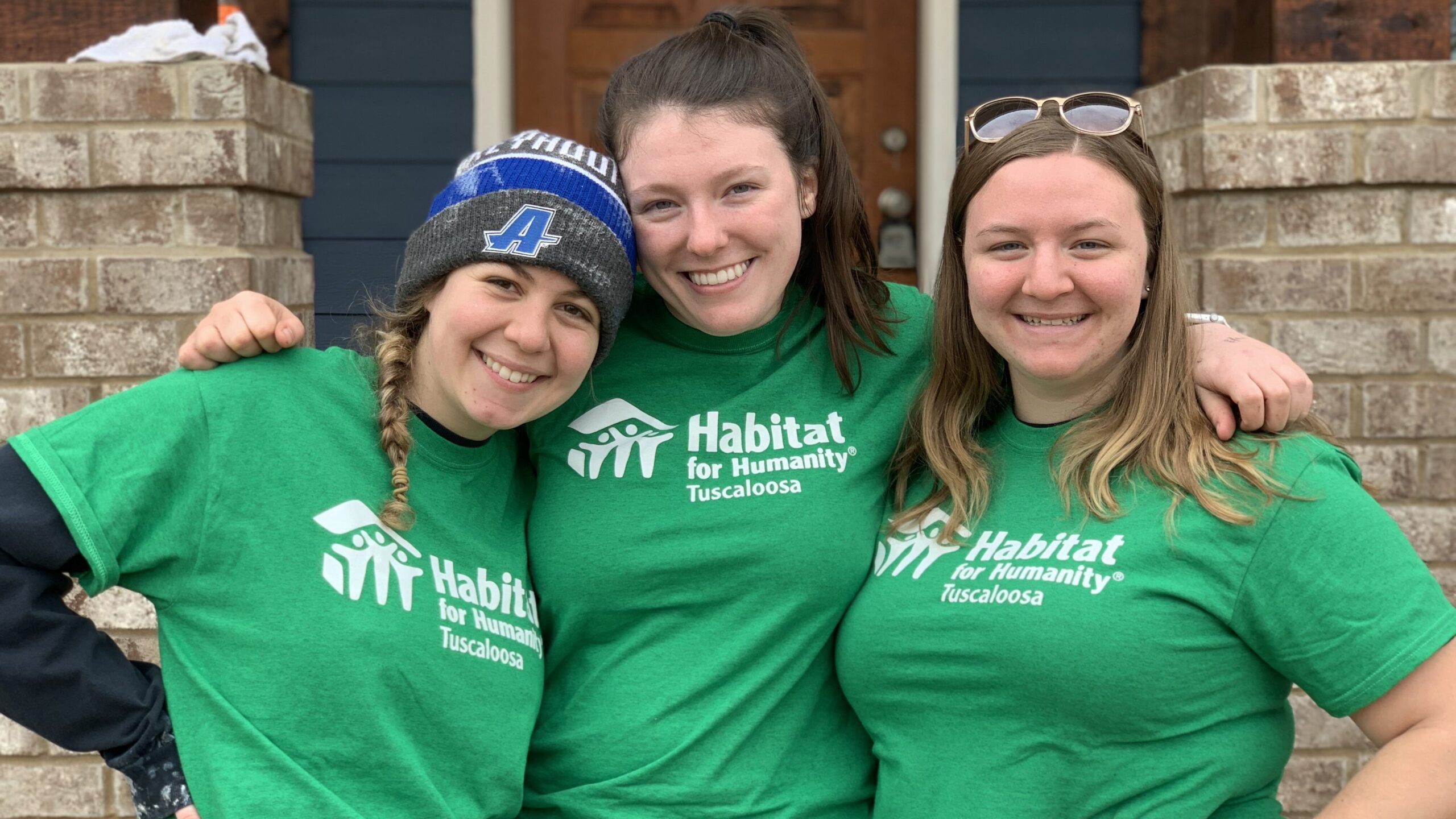 Three students dressed with their Habitat for Humanity shirts outside a volunteer location. 