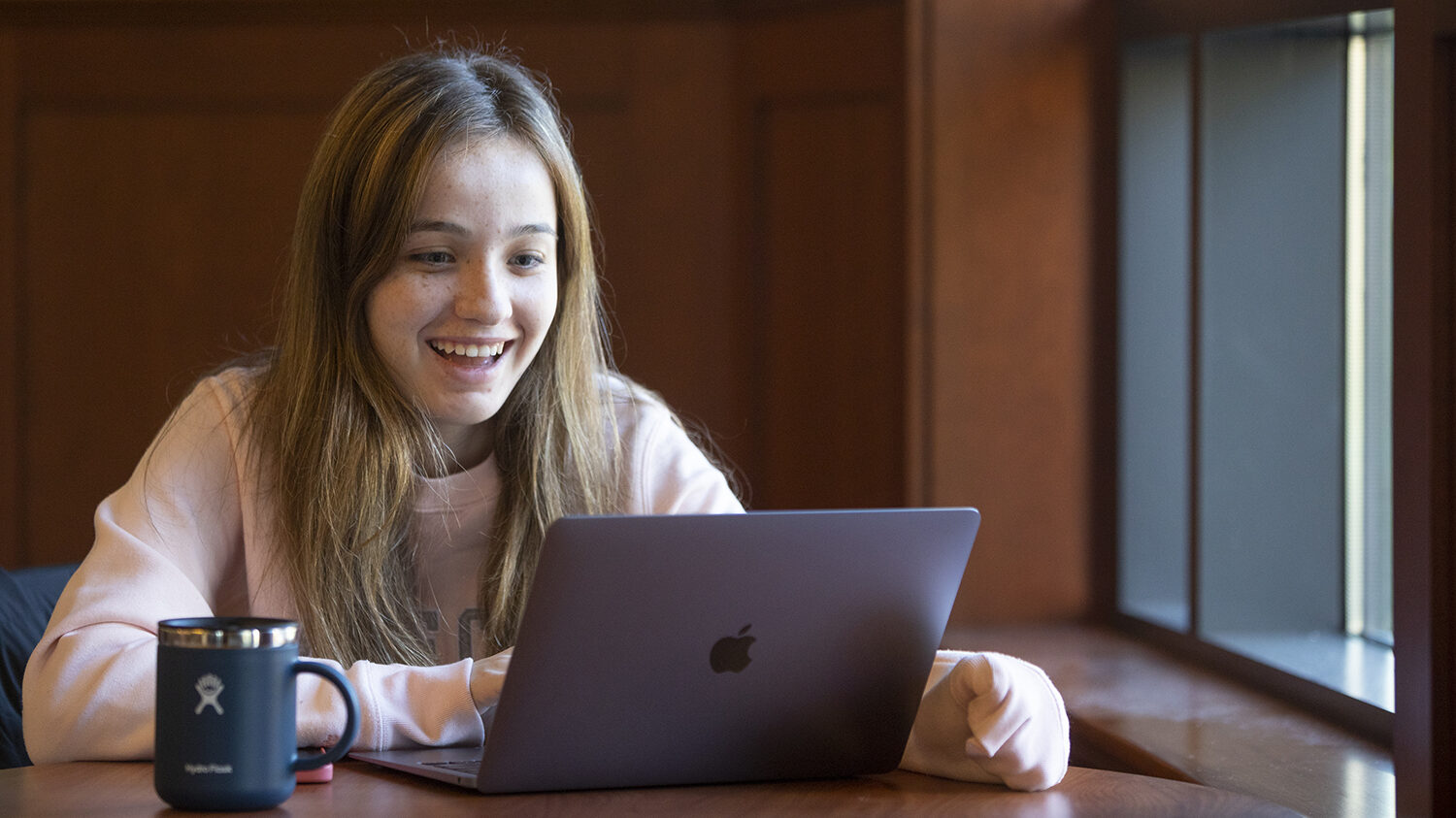 Assumption student smiling while doing work on their computer