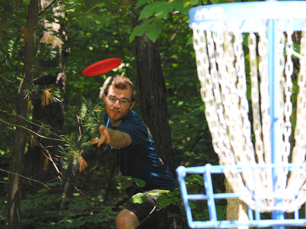 Assumption student throws a red frisbee during a game of disc golf