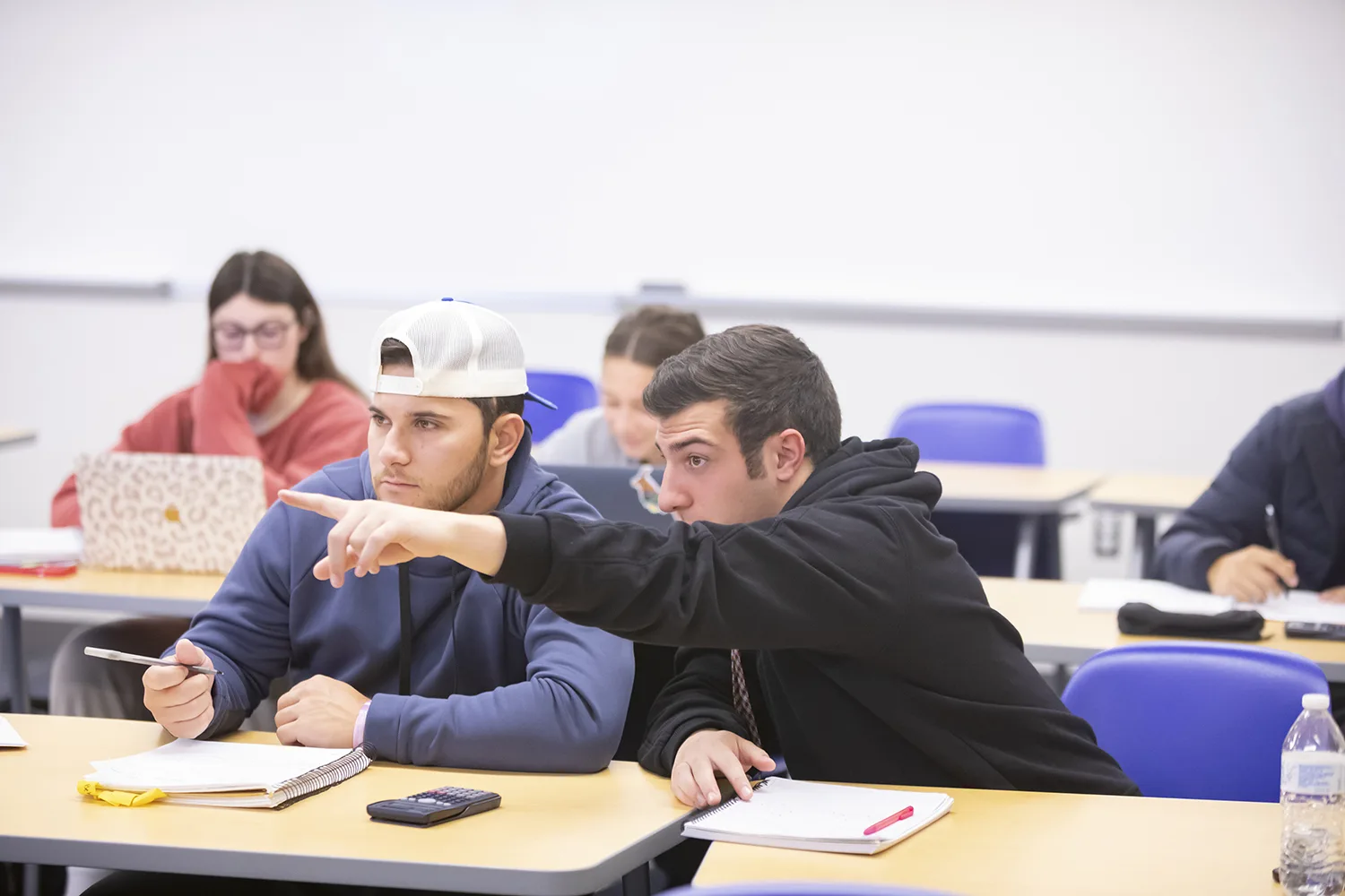 Two Assumption students in a classroom, one is pointing to something on the classroom board